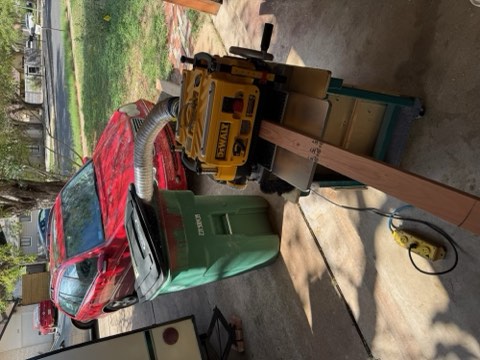 Red car, green container, yellow DeWalt tool, wooden plank, and power strip on concrete driveway.