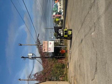 A forklift stands on a paved road near a signpost with a sign and a person in an orange vest.
