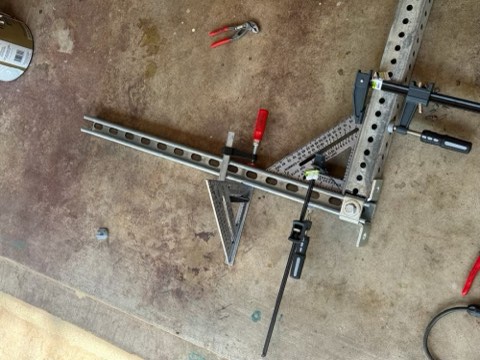 Metal fence frame with clamps, triangle ruler, and pliers on concrete floor.